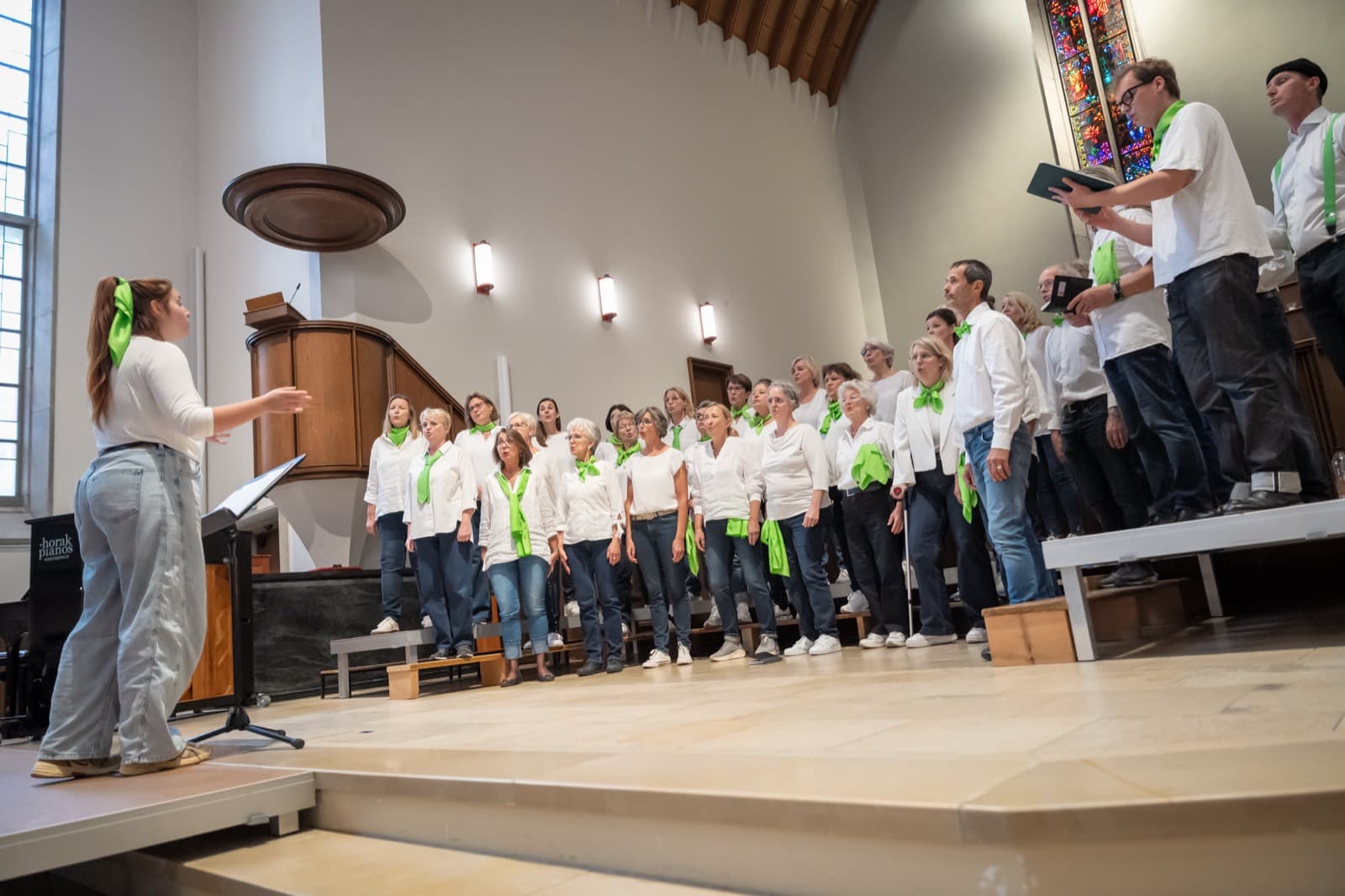 Chor beim Singen, die Chorleiterin dirigiert im Vordergrund